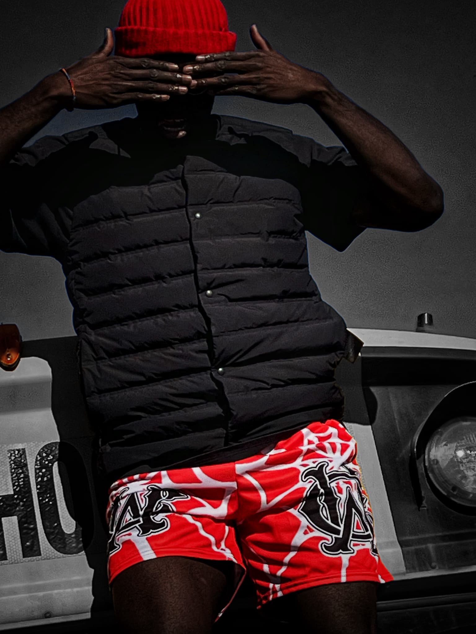 Model wearing OG Mesh Shorts in Red – Spider Web Edition, covering face in a high-contrast shot. Statement streetwear captured in raw energy.