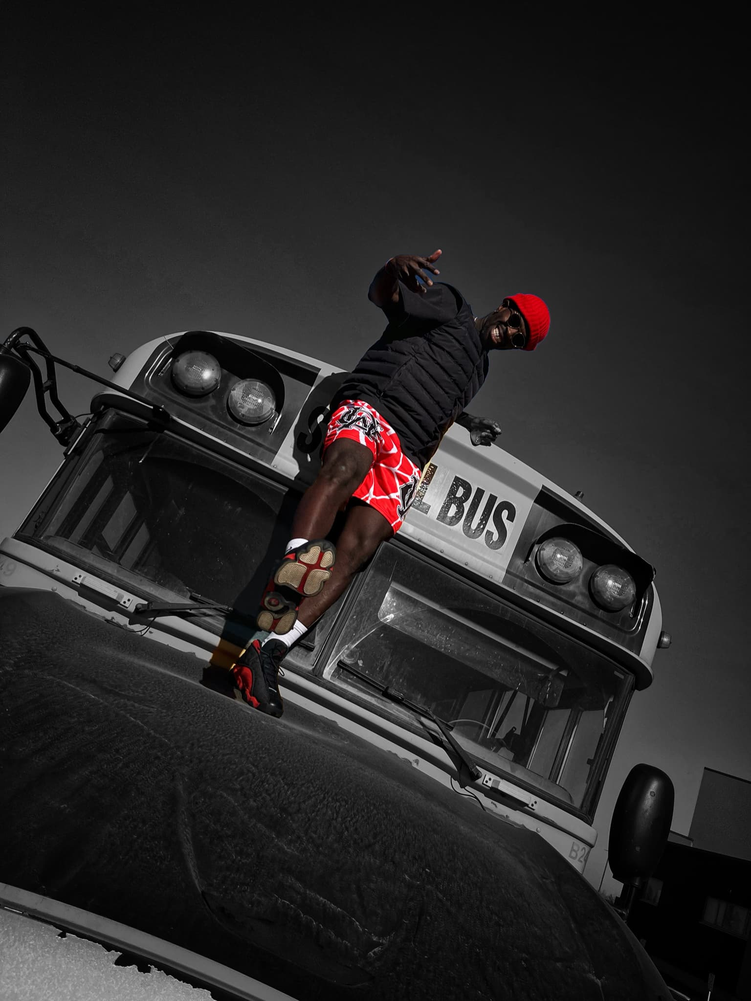 Model wearing OG Mesh Shorts in Red – Spider Web Edition, standing on top of a rugged bus. High-contrast streetwear shot with bold styling.