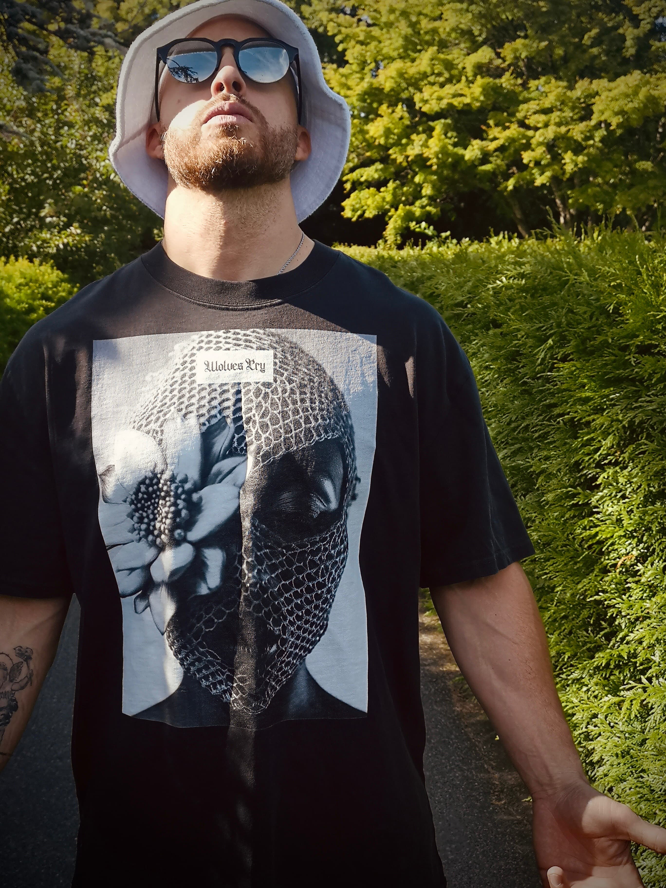 Model wearing the Wolves Cry Oversized Balaclava Tee in vintage black, styled with a bucket hat and sunglasses, showcasing the bold streetwear vibe.