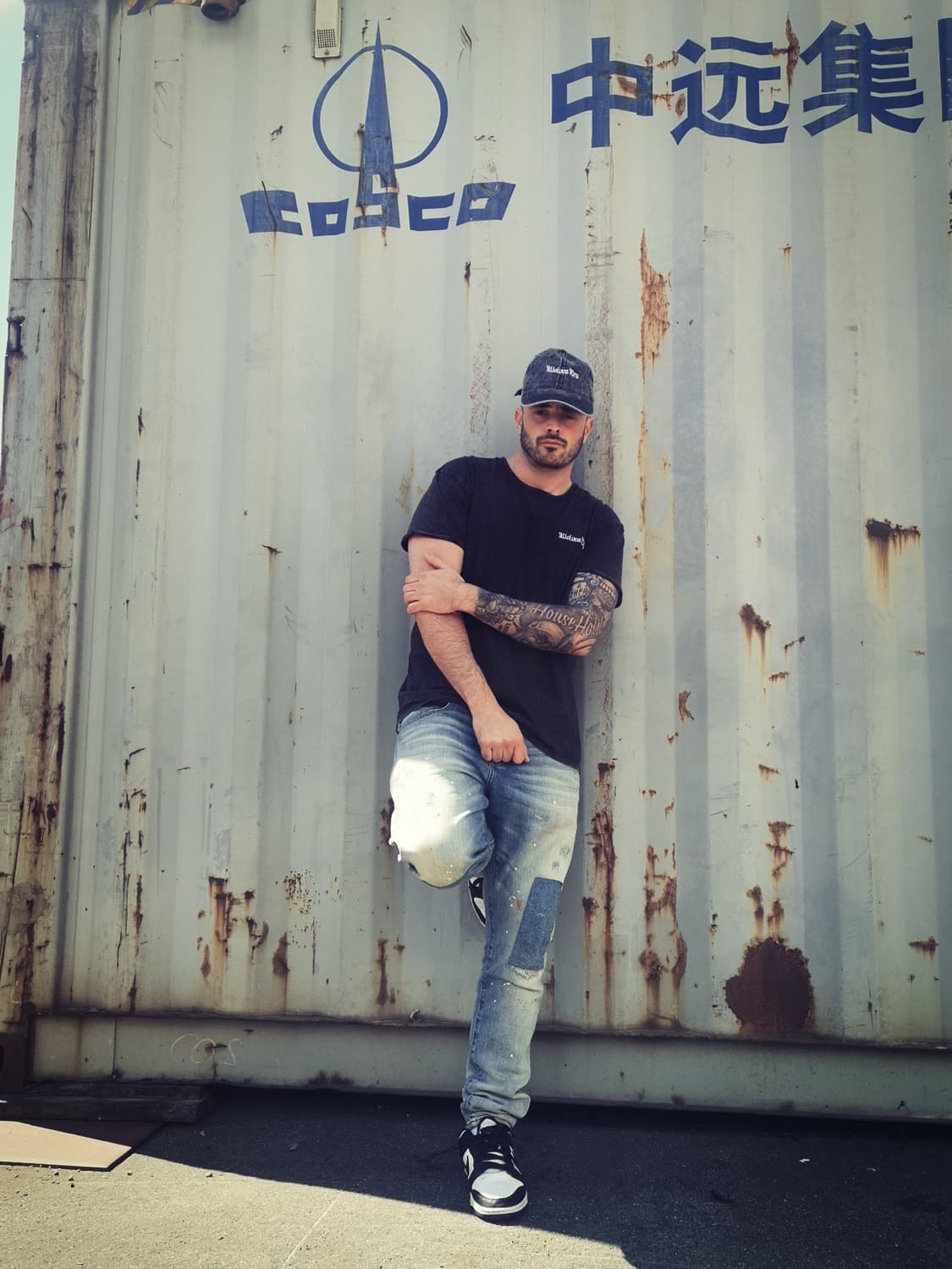 Model wearing the Wolves Cry Embroidered Denim Tee in black, paired with distressed denim and sneakers. A classic streetwear look with a vintage edge, captured against an industrial backdrop.