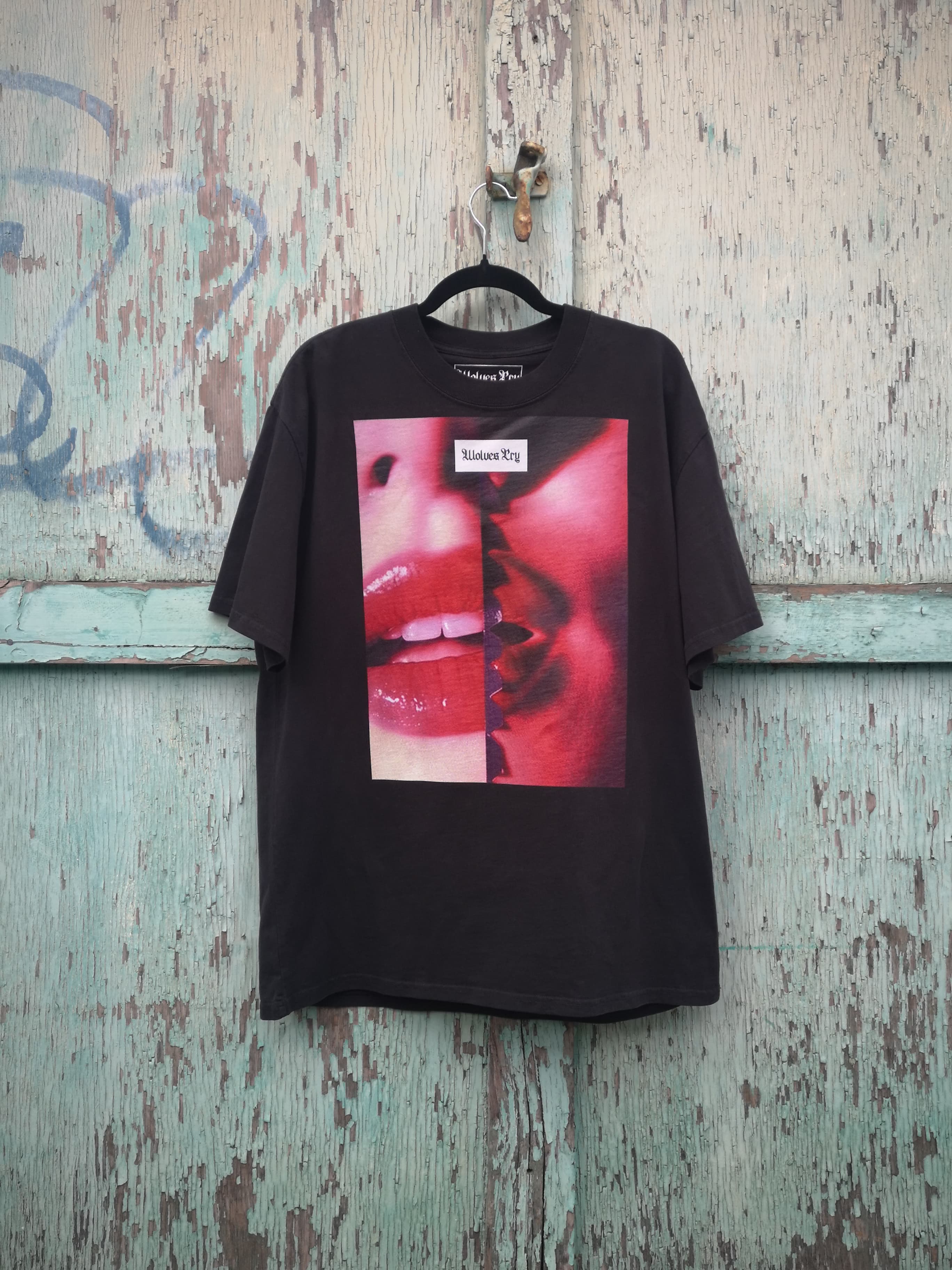 Wolves Cry Oversized Kiss Tee hanging against a raw, urban backdrop, showcasing the bold red and pink split design on heavyweight cotton.