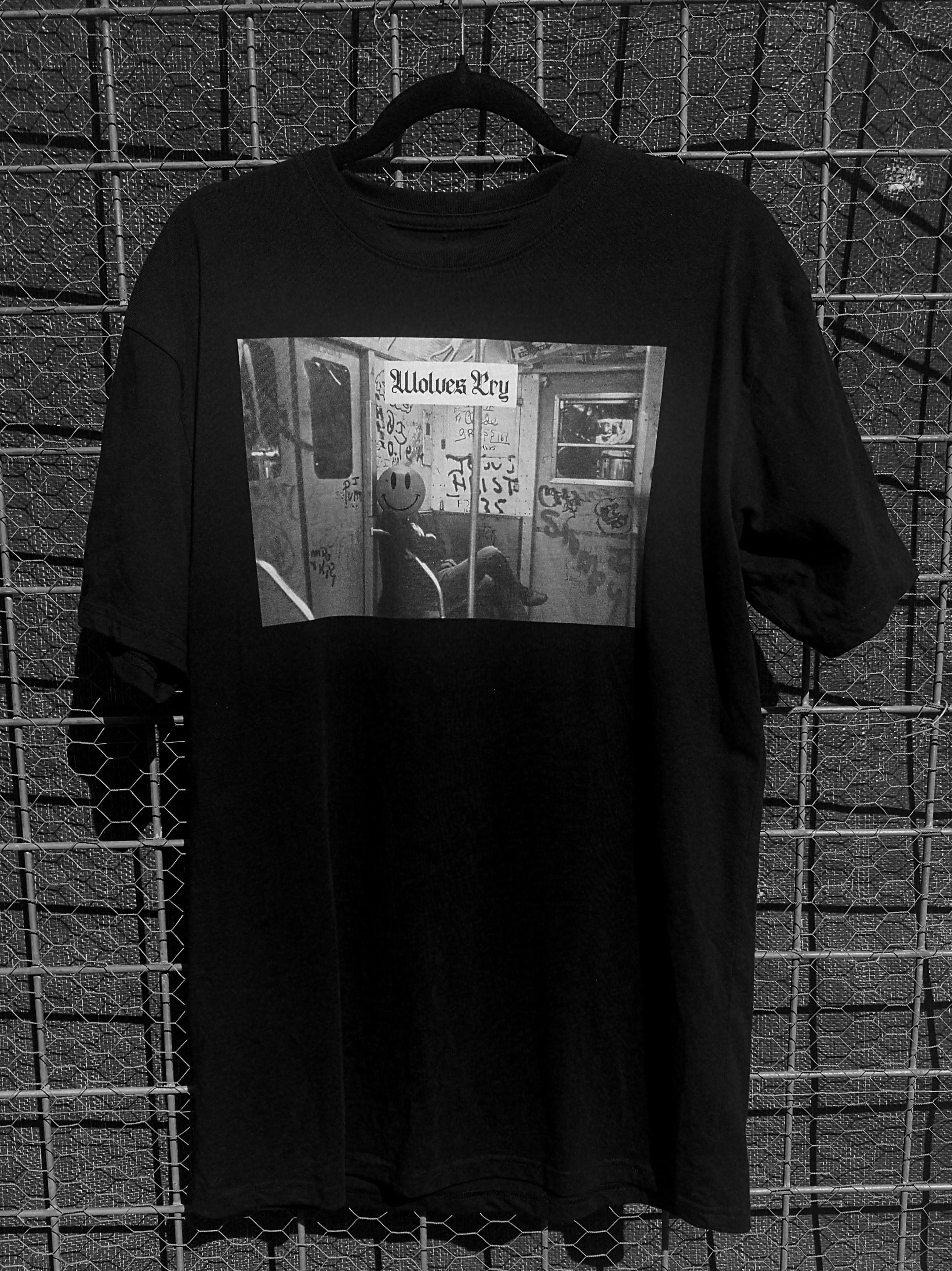 Wolves Cry Smiley Tee hanging against an industrial backdrop, highlighting the high-contrast graphic print and heavyweight fabric construction.